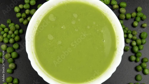 Fresh green pea puree soup in a white bowl and fresh green peas are on a black table photo