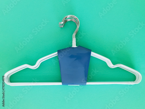 Metal white clothes hanger in packaging. Green background.
