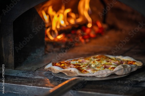 A pizzaiolo is baking a pizza in a wood-fired oven.