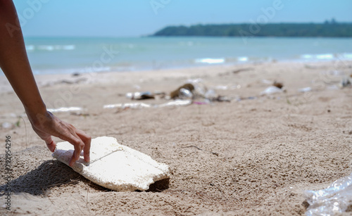 Woman hands pick up white foam sheet left on the sandy beach, Cleaning the beach, Collecting trash at the beach. Environmental Conservation concept.