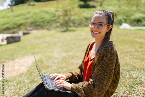 Smiling woman wearing sweater working with laptop in park