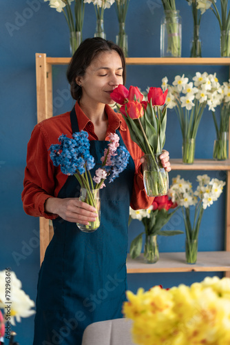 Attractive cute woman florist smelling red tulips flowers with eyes closed in flower shop
