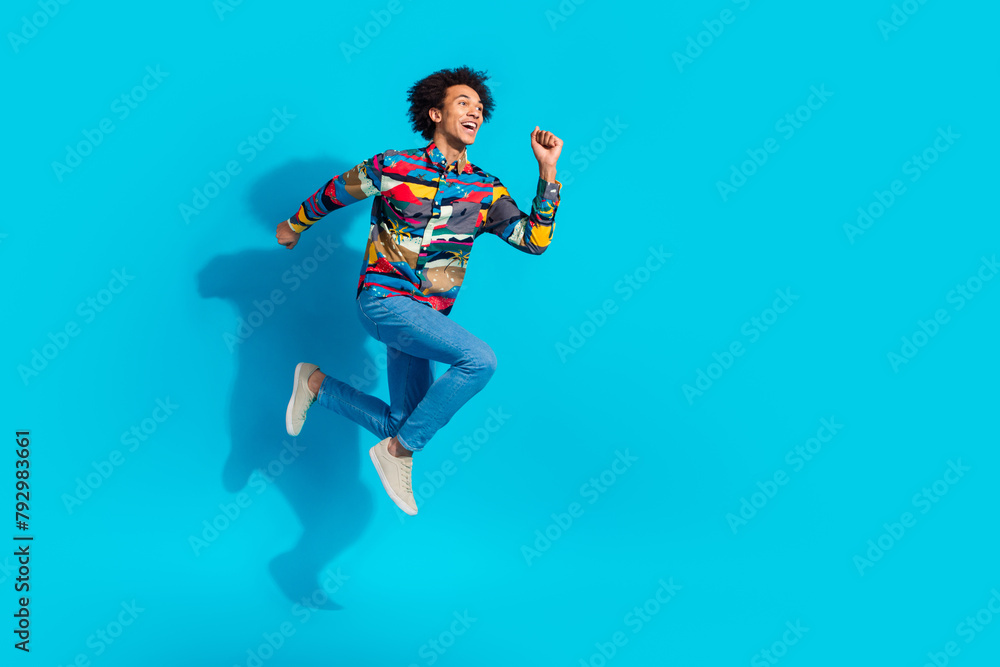 Full length photo of handsome young guy running hurry black friday dressed stylish print garment isolated on blue color background Full length photo of handsome young guy running hurry black friday dressed stylish print garment isolated on blue color background