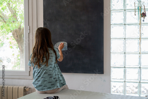 girl with a blue T-shirt and long hair sitting at a table and drawing on a blackboard in a space with lots of natural light