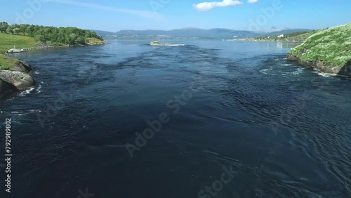 Video footage from a drone flying over the Saltstraumen whirlpool in Norway. The drone captures the rapid flow and twisting currents, with vibrant greenery and mountains in the backdrop