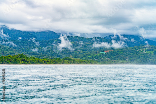 Tranquil ocean waters before a tropical coastline with clouds descending upon verdant hills. High quality photo. Uvita Puntarenas Province Costa Rica