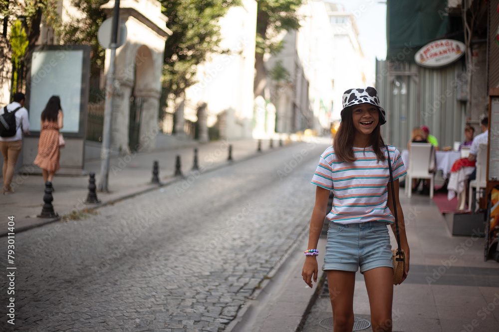 A beautiful girl in panama, with straw handbag, denim shorts and a striped T-shirt goes on the street of the city