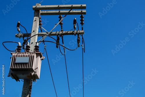 Electrical poles equipped with large power transformers The background is a bright blue sky.