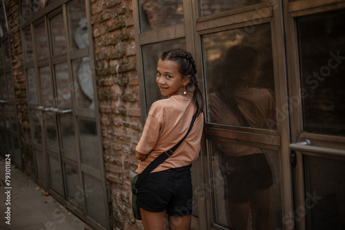 A beautiful girl with handbag, dressed denim black shorts and a T-shirt goes on the street of the city, posing against the background of brick walls and large windows