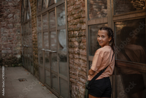 A beautiful girl with  handbag, dressed denim black shorts and a  T-shirt goes on the street of the city, posing against the background of brick walls and large windows © Вероника Зеленина