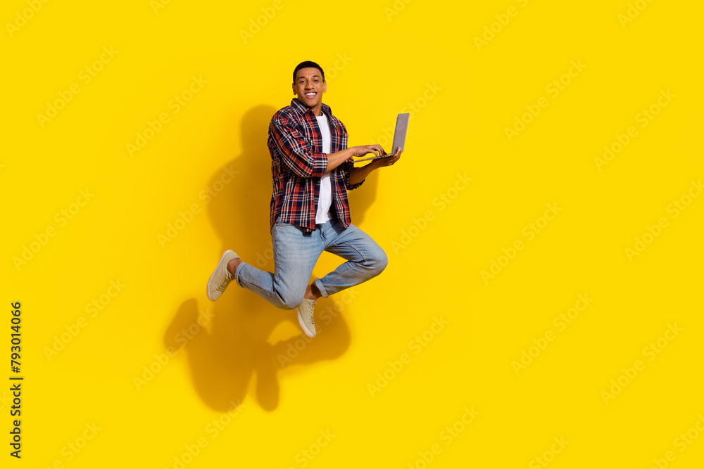 Full length photo of cheerful smart guy wear checkered shirt trousers jump with laptop in hands isolated on vibrant color background Full length photo of cheerful smart guy wear checkered shirt trousers jump with laptop in hands isolated on vibrant color background