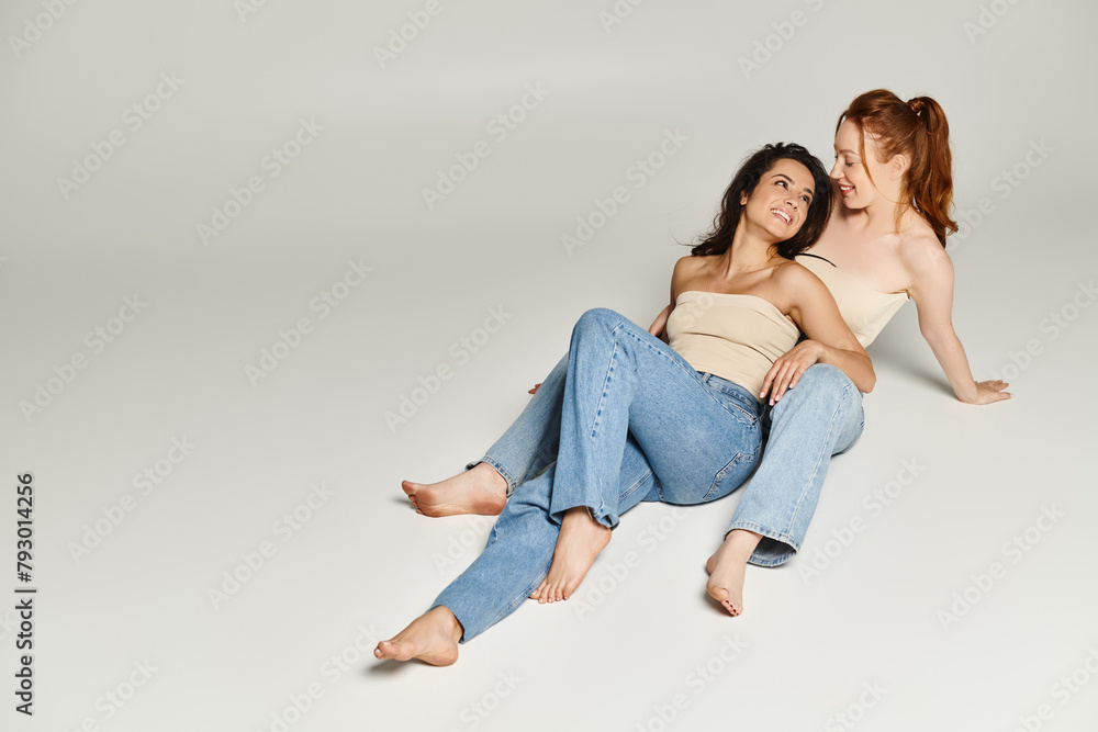 Two elegant women, a loving lesbian couple, sit gracefully on the floor together. Two elegant women, a loving lesbian couple, sit gracefully on the floor together.