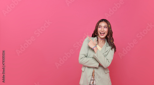 Happy young Asian teen woman standing with her pointing finger isolated on pink background with copy space.