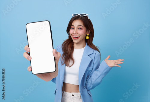 Beautiful Asian business woman showing smartphone mockup of blank screen isolated on blue background.