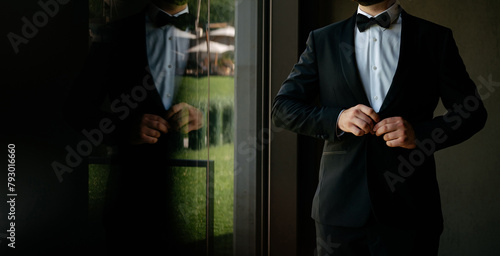 groom in elegant tuxedo arranging his jacket.