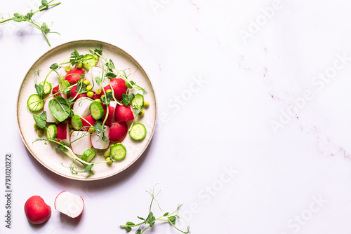 Fresh spring salad witred radish, cucumber,aromatic herbs and olive oil on white marble table top view. Healthy diet food concept.
