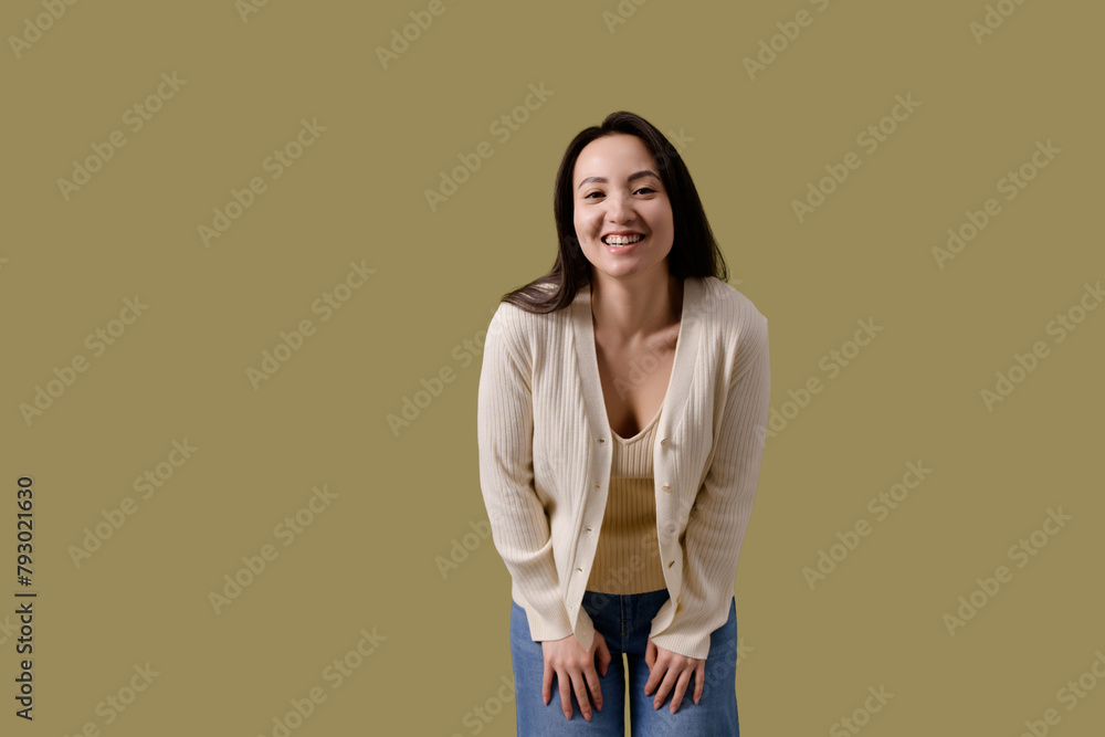 Obraz premium Cheerful brunette asian woman in casual clothes looking at camera isolated on green 