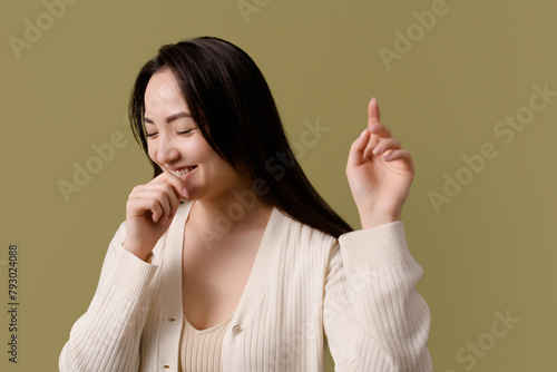 Portrait of cheerful asian woman with closed eyes isolated on green 