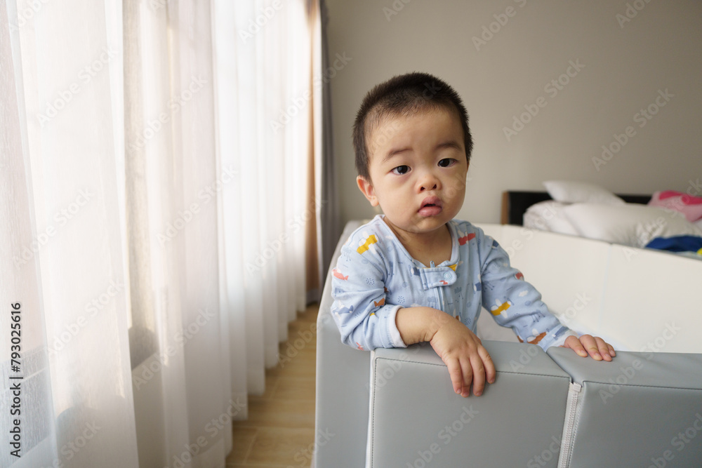 Sleepy Asian baby boy standing at window after waking up Sleepy Asian baby boy standing at window after waking up