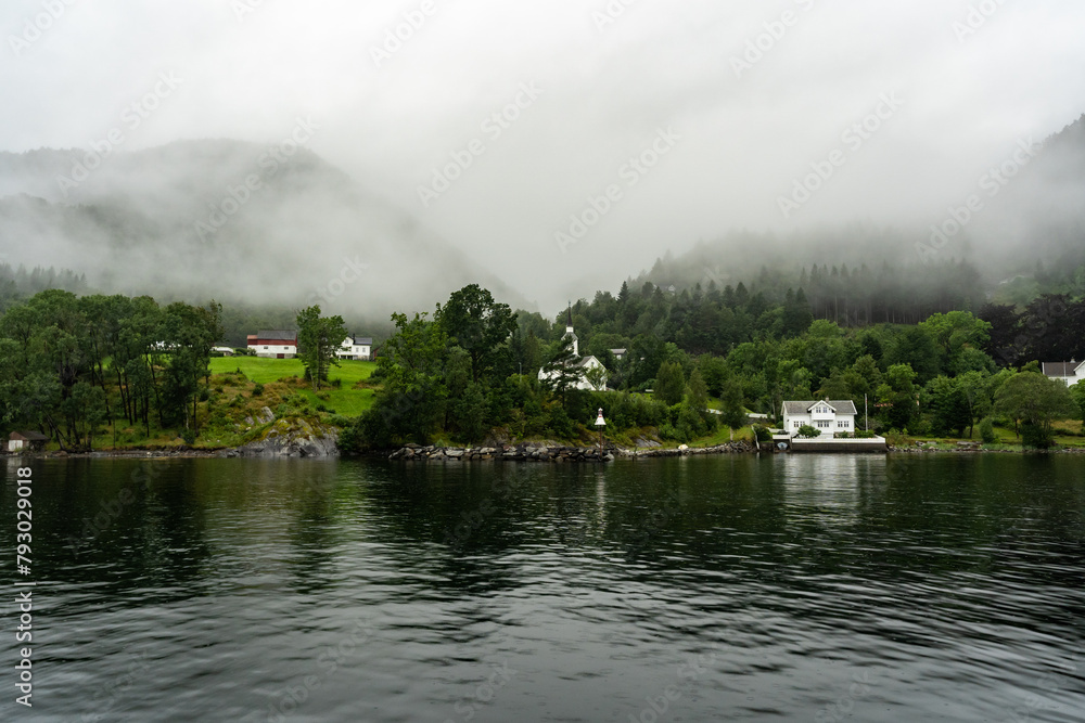 Norwegian fjords in fog. Village on the shore. Church. Northern mountains in foggy clouds. Beautiful reflections on calm water. Amazing stunning views of the Scandinavian Northern European mountains. Norwegian fjords in fog. Village on the shore. Church. Northern mountains in foggy clouds. Beautiful reflections on calm water. Amazing stunning views of the Scandinavian Northern European mountains.