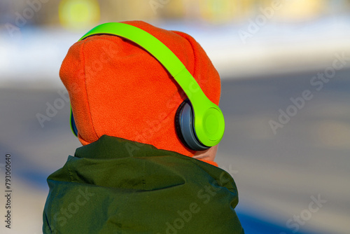 Back view stylish woman in a bright orange hat wearing wireless green headphones listening to music while walking. Selective focus.Relax, rest.