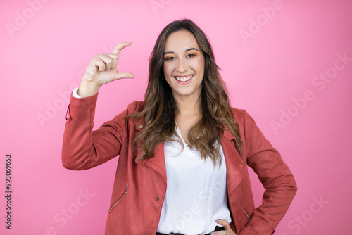 Young beautiful woman wearing casual jacket over isolated pink background smiling and confident gesturing with hand doing small size sign with fingers . Measure concept.