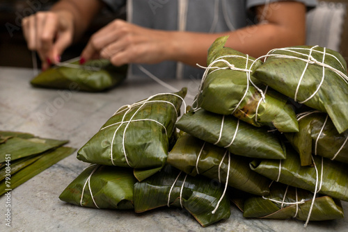 Woman's hands tying a hallaca or tamale in a banana leaf. Traditional food