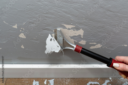 Removing silicone paint from a wall damaged by dog claws using a paint and adhesives scraper, womans hand visible.