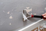 Removing silicone paint from a wall damaged by dog claws using a paint and adhesives scraper, womans hand visible.