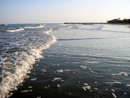 Calm waves roll in on the wide evening sea beach under a clear sky