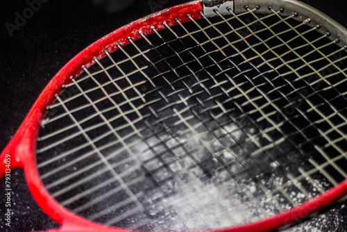 Red tennis racket strings close up with black background and white powder