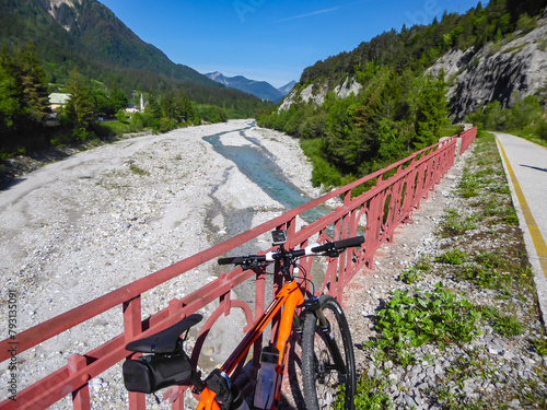 Mountain bike mtb leaning against iron bars of bridge along the Alpe Adria trail in Friuli-Venezia Giulia, Italy, Europe. Braided river Tagliamento running through wild mountainous landscape. Awe