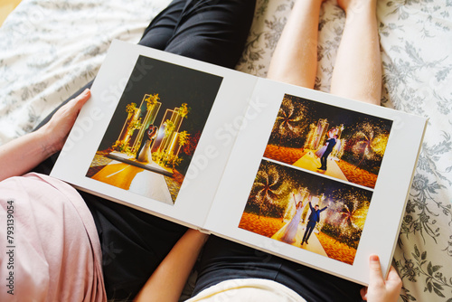 Billede på lærred Mom and daughter flipping through a wedding photo book on the bed