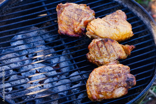Chicken thighs cooking on a charcoal grill with hot coals in view. Selective focus, background blur, foreground blur