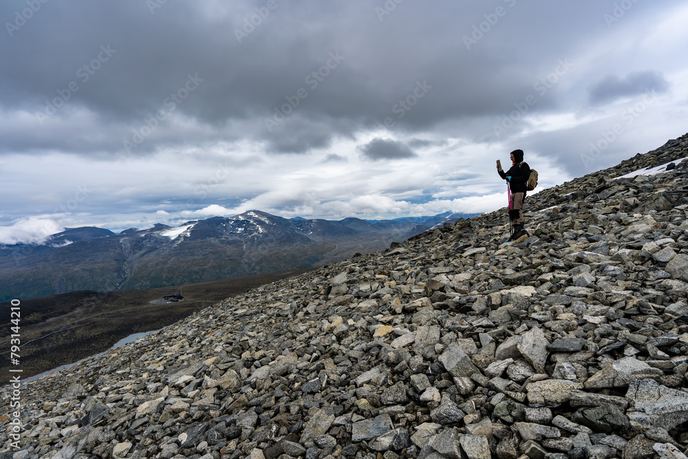 Male traveler in the snowy mountains of Norway. Young Man making photo or selfie on trekking hiking with Scandinavian sticks. Rest in beautiful mountainous area with glaciers. Amazing northern view.