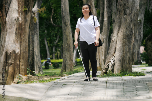 Woman with blindness disability walking on sidewalk contain tactile paving guide blocks using long white cane or blind cane a mobility tool to detect objects in the path for vision impairment people © Chansom Pantip