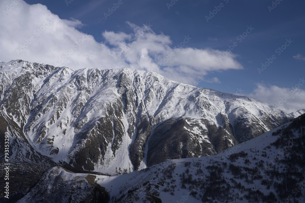 Obraz premium The snow-covered peaks of the mountain range under a sky, Gergeti Trinity Church, Stepantsminda, Georgia