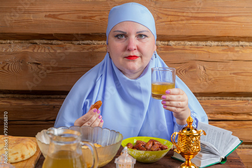 A Muslim woman in a blue hijab at the table eats a date and suhoor for the holiday of Eid al-Fitr
