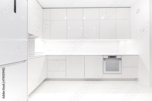 Front view of a modern luxury trendy snow white kitchen with many cabinets, glossy lacquered facades and integrated handle