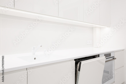 Modern white kitchen interior with acrylic countertop and built in stone sink and opened door of washing machine, luxury monochrome design, image with selective focus
