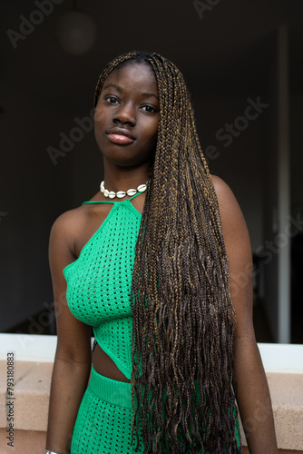 A poised young black woman with intricate braids wears a vibrant green crochet dress, exuding confidence and style