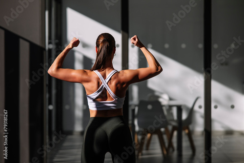A strong female athlete showcases her toned back muscles while flexing in a modern home environment, displaying fitness and strength photo