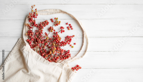 A bouquet of twigs with red sea buckthorn berries, Shepherdia argentea in a linen bag on a white painted wooden surface close-up, copy space. Alternative medicine photo