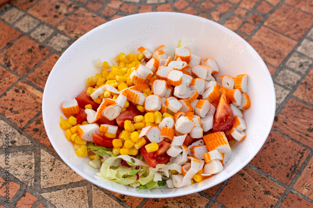 A vibrant salad, featuring crab sticks, corn, and crisp green lettuce, arranged on a white plate, looks delicious