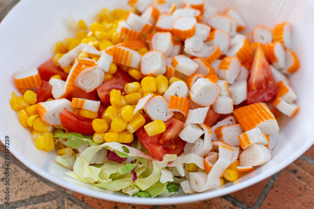 Featuring crab sticks, sweet corn, and green lettuce, a colorful salad is elegantly presented on a white plate