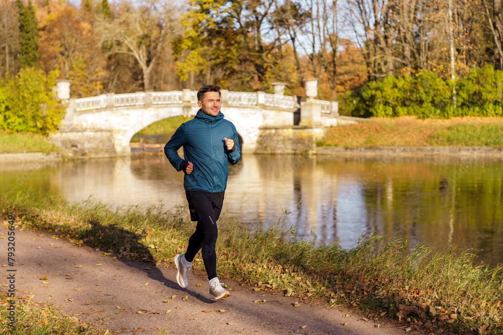 Fototapeta premium A man enjoys a run in a picturesque park, with an ornate bridge and reflective water enhancing the scene.