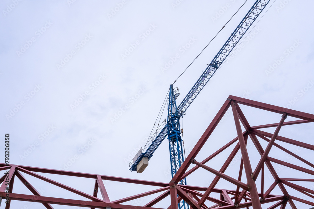 Geometric composition of red metal beams and a blue crane in a modern construction against a clear sky with copy space Geometric composition of red metal beams and a blue crane in a modern construction against a clear sky with copy space