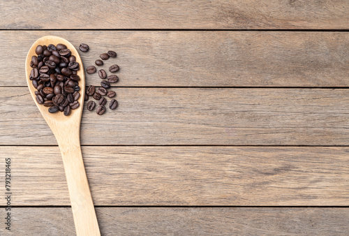 Coffee beans on a spoon over wooden table with copy space