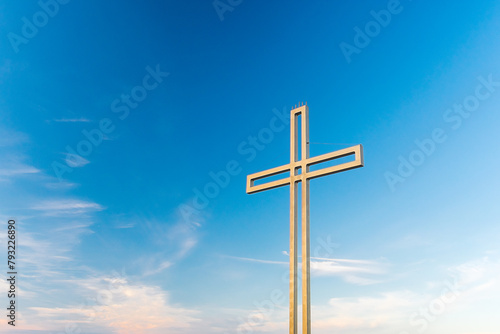 Golden cross against a background of blue sky with clouds. A minimalistic view of a gold-colored cross against the sky.