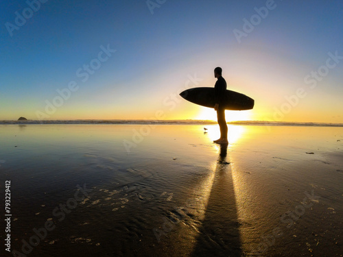 Surfer man standing in the beach at sunset. New Zealand